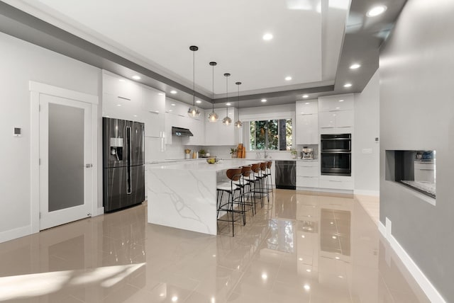 kitchen featuring decorative light fixtures, white cabinetry, a breakfast bar area, black appliances, and a spacious island