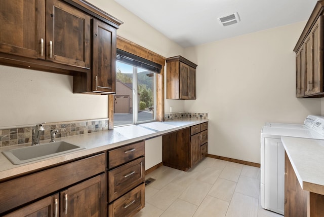 kitchen with light tile patterned flooring, tasteful backsplash, sink, dark brown cabinetry, and washer and clothes dryer