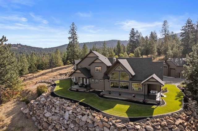 back of property with a wooded view, a patio, and a lawn