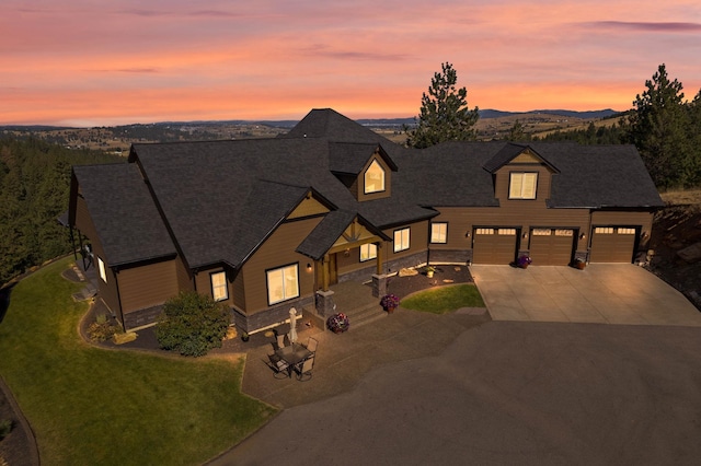 view of front of home featuring a lawn, concrete driveway, a shingled roof, and stone siding