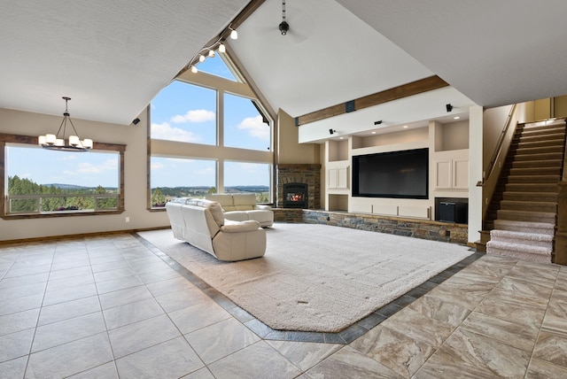 living room with high vaulted ceiling, a notable chandelier, a healthy amount of sunlight, and a warm lit fireplace