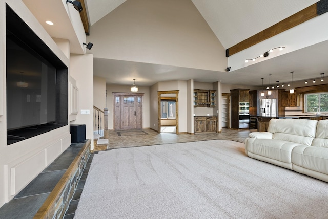 carpeted living area featuring a sink, track lighting, high vaulted ceiling, and baseboards
