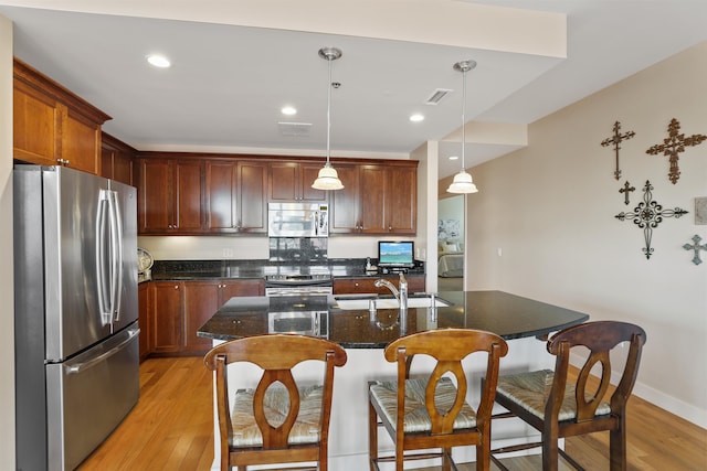 kitchen featuring pendant lighting, light wood-type flooring, sink, a center island with sink, and appliances with stainless steel finishes