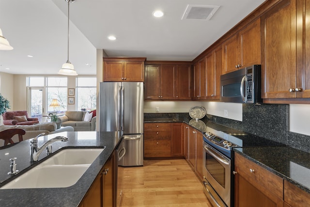 kitchen featuring hanging light fixtures, sink, appliances with stainless steel finishes, dark stone counters, and light hardwood / wood-style floors