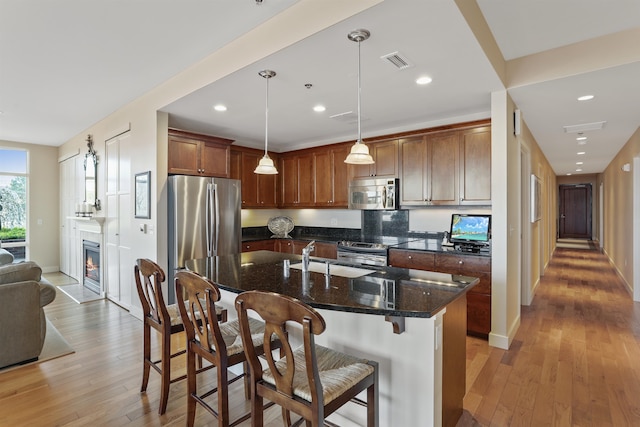 kitchen featuring an island with sink, appliances with stainless steel finishes, pendant lighting, and light hardwood / wood-style flooring