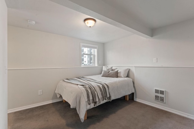 bedroom with dark carpet, beamed ceiling, and heating unit