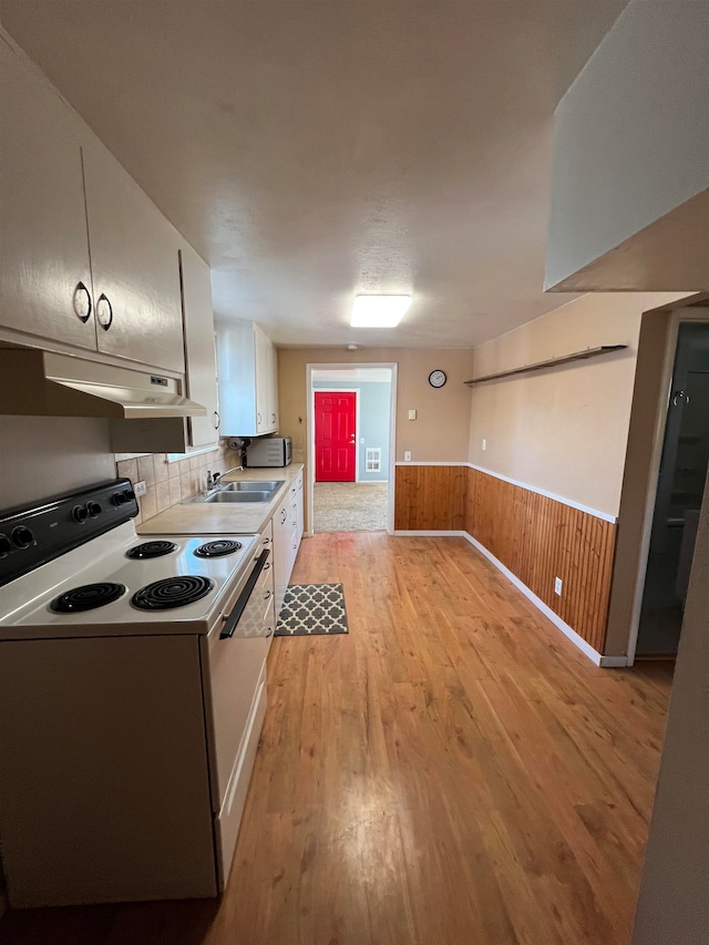 kitchen with white cabinets, light wood-type flooring, white range with electric stovetop, wooden walls, and sink