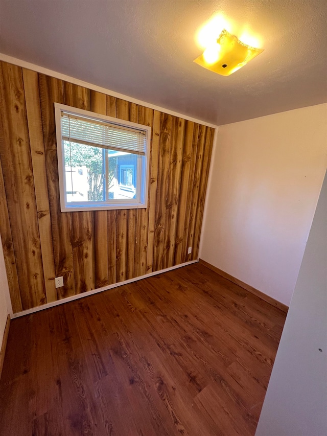 unfurnished room featuring hardwood / wood-style flooring, wood walls, and a textured ceiling