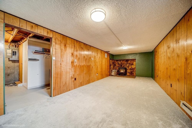 basement with a stone fireplace, light colored carpet, wood walls, and a baseboard heating unit