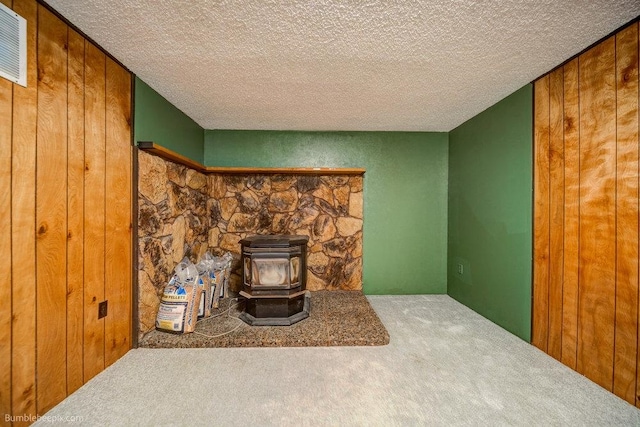 room details featuring a wood stove, wood walls, a textured ceiling, and carpet flooring