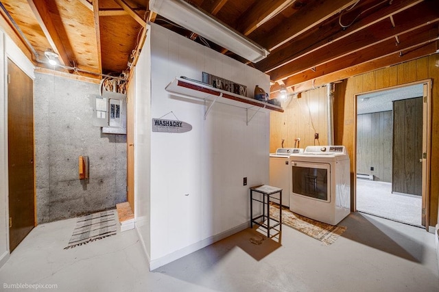 basement featuring washing machine and dryer, wood walls, baseboard heating, and electric panel