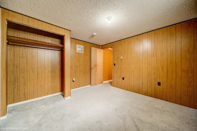 unfurnished bedroom featuring light carpet, wood walls, a closet, and a textured ceiling