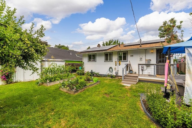 rear view of property featuring a lawn, solar panels, and a wooden deck