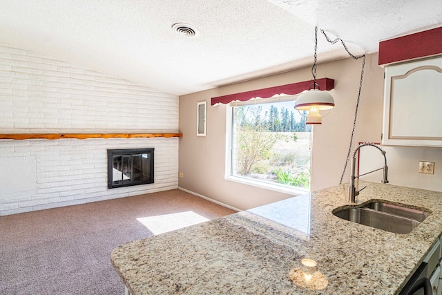 kitchen featuring sink, brick wall, a textured ceiling, light carpet, and vaulted ceiling