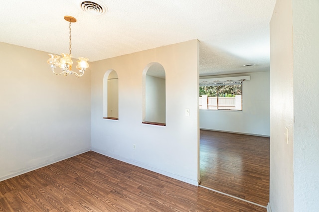 empty room with a textured ceiling, dark wood-type flooring, and a chandelier