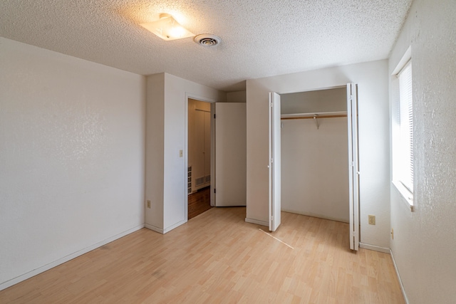 unfurnished bedroom featuring a textured ceiling, light wood-type flooring, a closet, and multiple windows