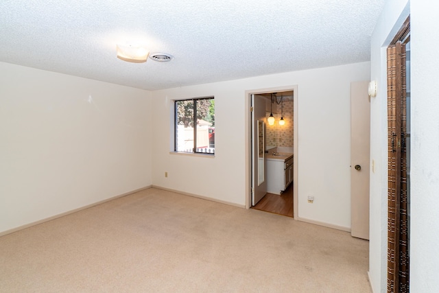 unfurnished bedroom with light colored carpet, a textured ceiling, and ensuite bathroom