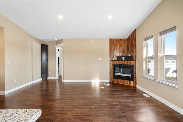 unfurnished living room featuring a large fireplace, dark hardwood / wood-style flooring, and plenty of natural light