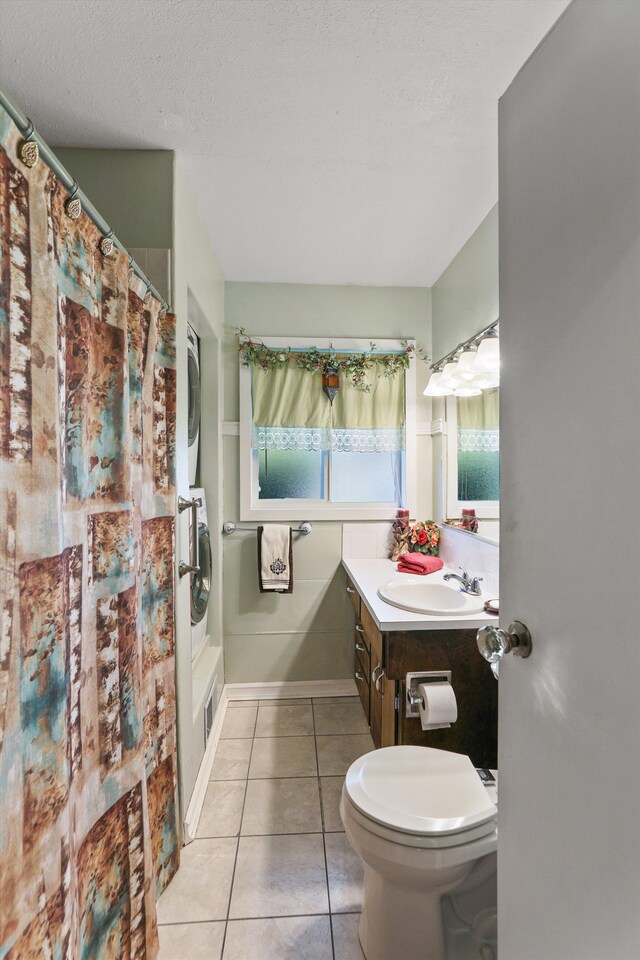 bathroom with a textured ceiling, stacked washer / dryer, tile patterned floors, vanity, and toilet