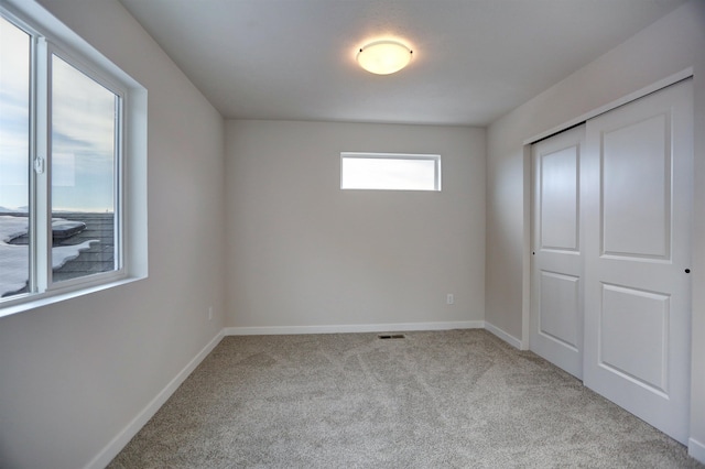 unfurnished bedroom with multiple windows, light carpet, and a closet