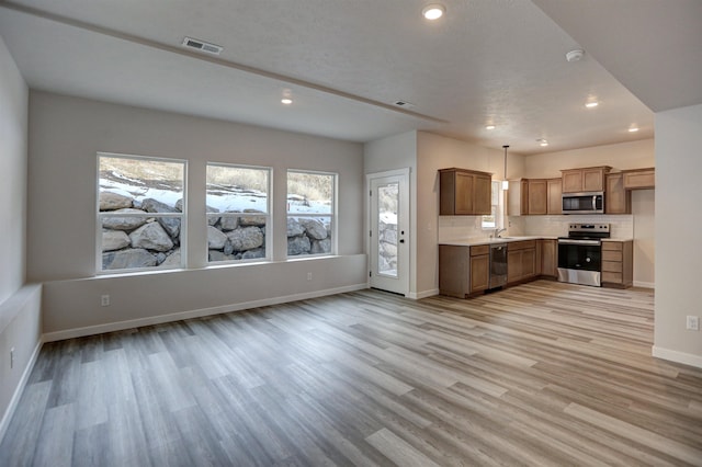 kitchen with stainless steel appliances, hanging light fixtures, sink, and light wood-type flooring