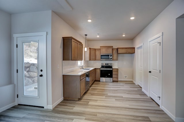 kitchen featuring sink, hanging light fixtures, backsplash, stainless steel appliances, and light hardwood / wood-style floors