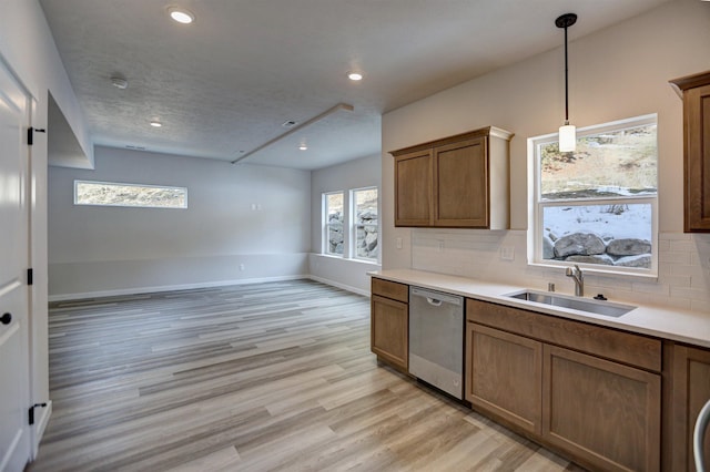 kitchen with sink, backsplash, light hardwood / wood-style floors, decorative light fixtures, and stainless steel dishwasher