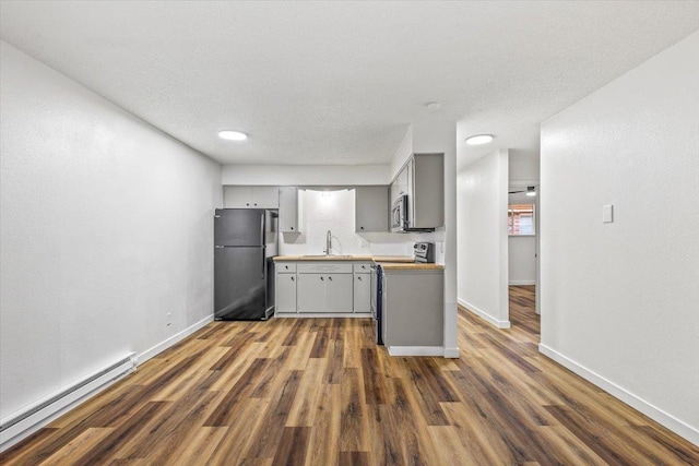 kitchen with a textured ceiling, dark wood-type flooring, a baseboard radiator, gray cabinetry, and appliances with stainless steel finishes