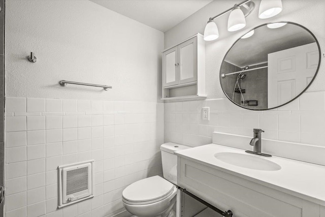 bathroom featuring heating unit, tile walls, vanity, and toilet