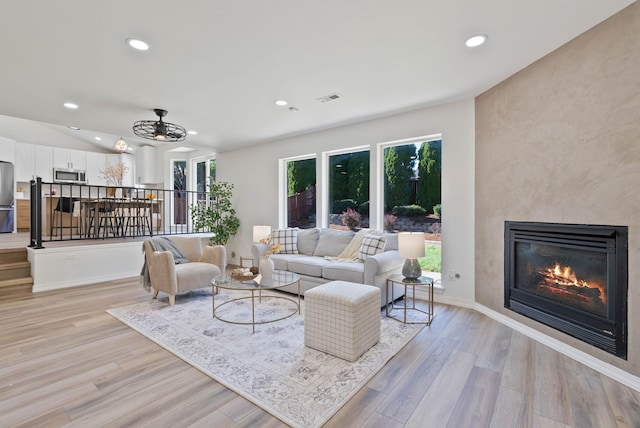 living room with ceiling fan, a fireplace, and light hardwood / wood-style flooring