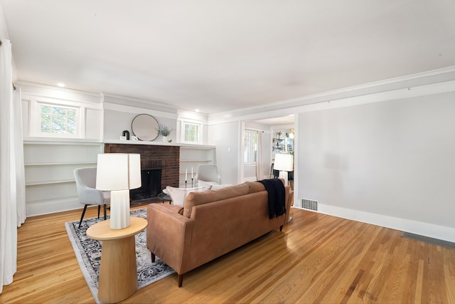 living room featuring crown molding, a brick fireplace, and light wood-type flooring