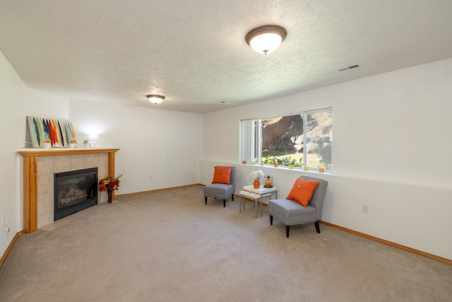 sitting room with carpet floors, a textured ceiling, and a tiled fireplace