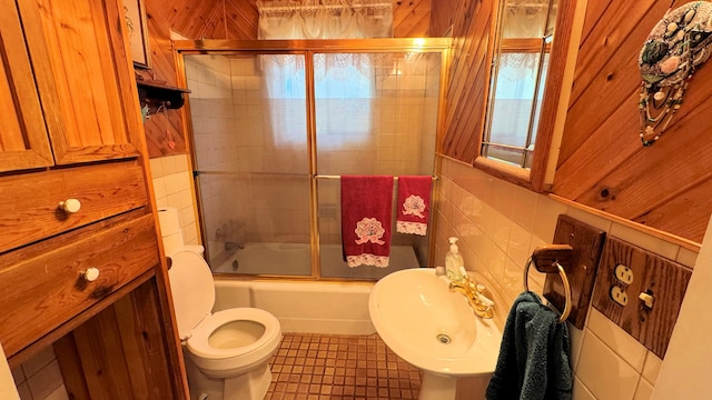 full bathroom with wood walls, tile patterned flooring, bath / shower combo with glass door, toilet, and sink