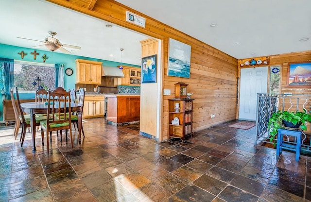 kitchen featuring pendant lighting, wood walls, wall chimney range hood, decorative backsplash, and ceiling fan