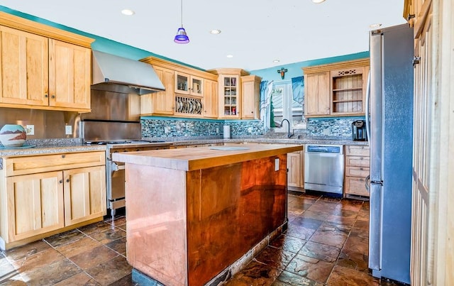 kitchen with wall chimney exhaust hood, pendant lighting, a center island, appliances with stainless steel finishes, and light brown cabinets