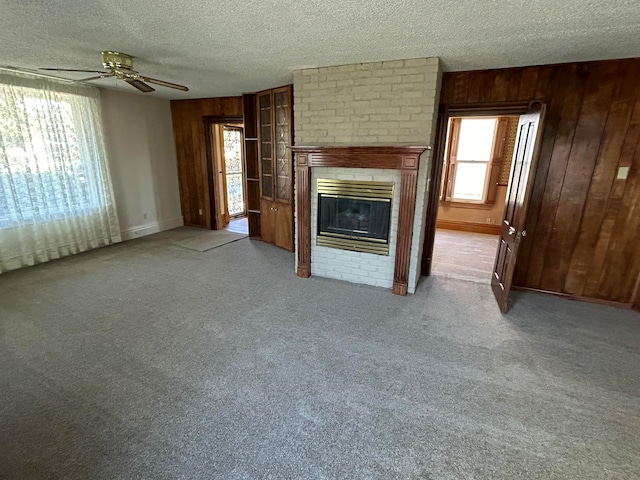 unfurnished living room with wood walls, ceiling fan, a fireplace, and a textured ceiling