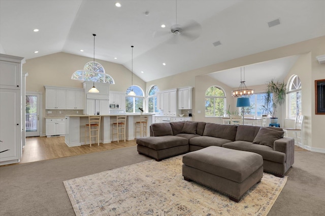 living room with ceiling fan with notable chandelier, high vaulted ceiling, and light hardwood / wood-style flooring