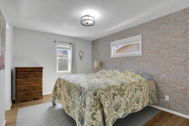 bedroom with brick wall and light hardwood / wood-style floors