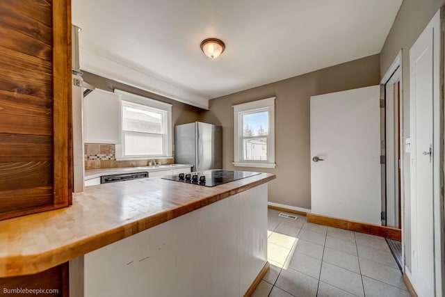 kitchen with decorative backsplash, plenty of natural light, stainless steel refrigerator, and wood counters