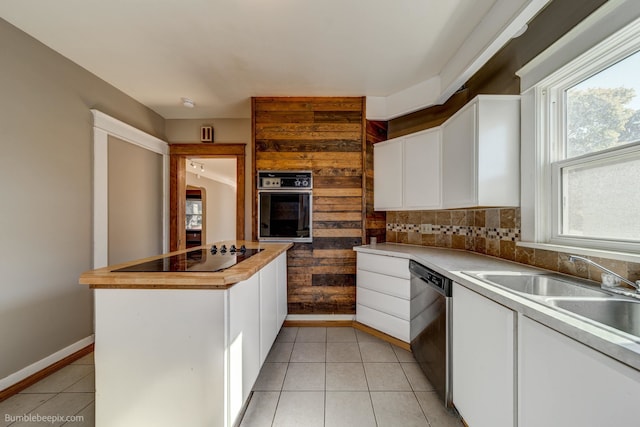 kitchen featuring a healthy amount of sunlight, black appliances, wooden walls, and white cabinetry