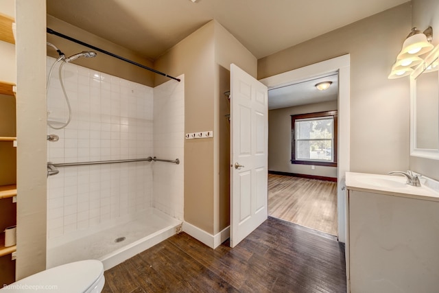 bathroom featuring a tile shower, hardwood / wood-style flooring, vanity, and toilet