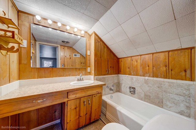 bathroom featuring lofted ceiling, a tub, wooden walls, and vanity