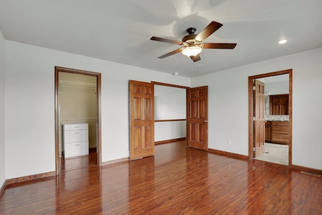 unfurnished bedroom with ceiling fan, hardwood / wood-style floors, ensuite bathroom, and a walk in closet