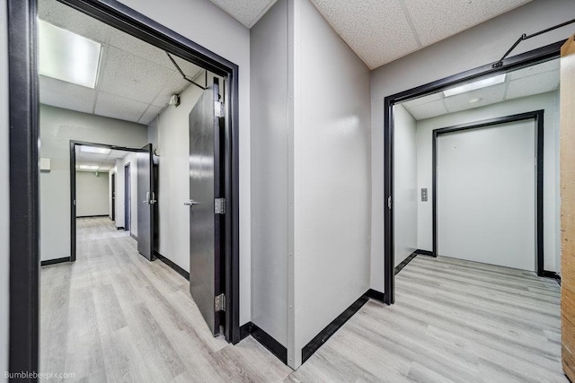 corridor with light wood-type flooring and a paneled ceiling