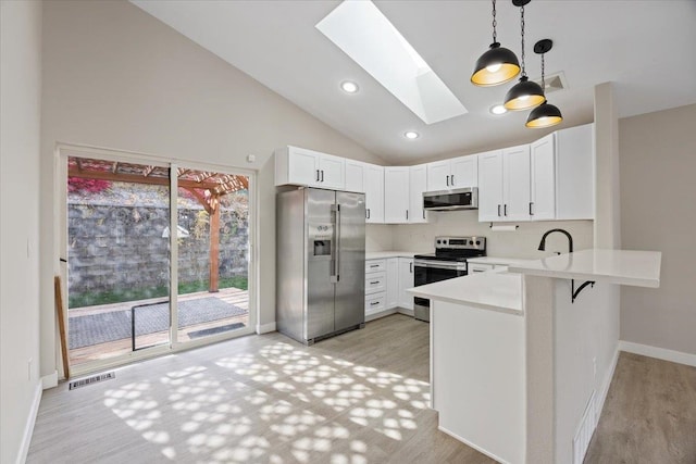 kitchen with a skylight, decorative light fixtures, stainless steel appliances, kitchen peninsula, and white cabinetry