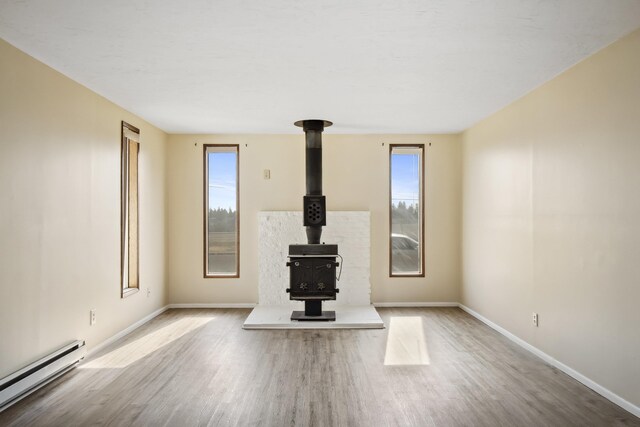 unfurnished living room with wood-type flooring, a wood stove, and a baseboard radiator