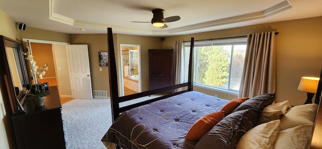 bedroom with ceiling fan, a raised ceiling, ensuite bath, and carpet