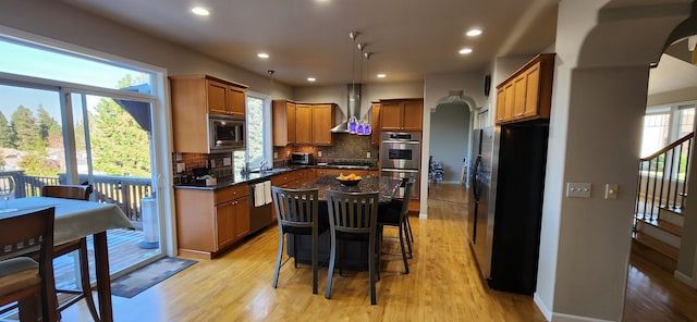 kitchen with wall chimney exhaust hood, tasteful backsplash, decorative light fixtures, appliances with stainless steel finishes, and a center island