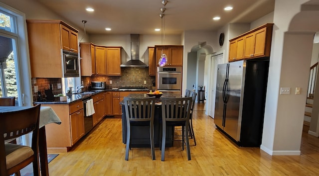 kitchen with decorative light fixtures, stainless steel appliances, wall chimney exhaust hood, and a healthy amount of sunlight