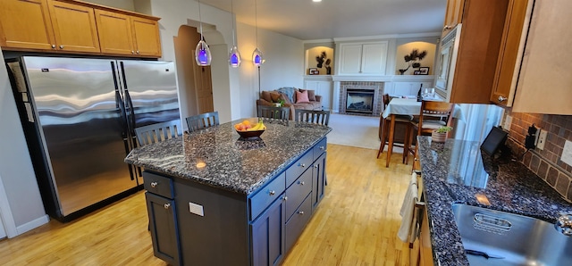 kitchen with stainless steel fridge, a kitchen island, a fireplace, and light hardwood / wood-style floors